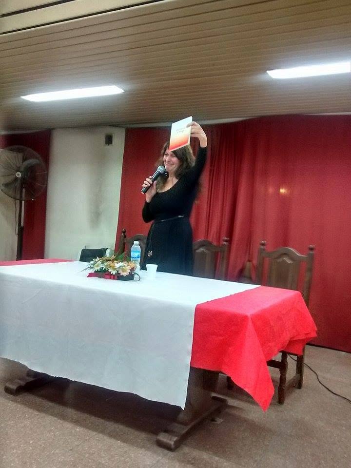 Patricia sostiene un ejemplar de De carne y fuego mientras habla al micrófono